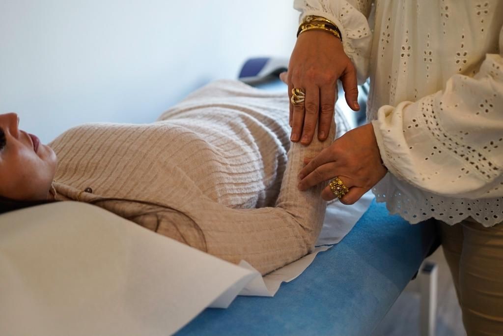 Person lying on an examination table receiving a therapeutic treatment on their arm from another individual.